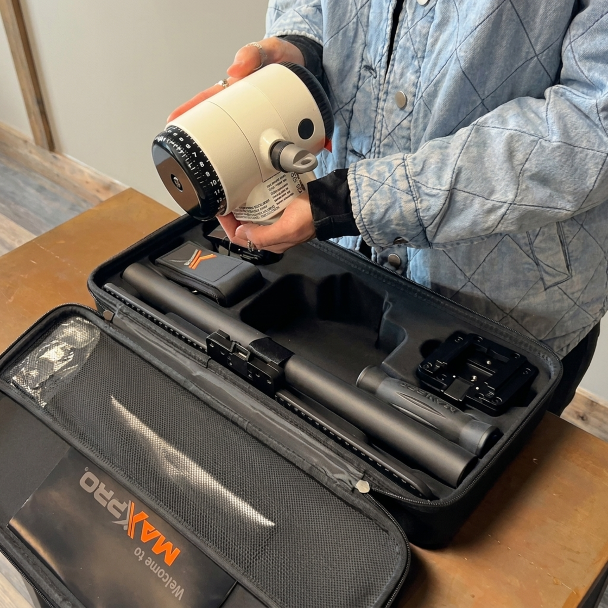 Person holding a drill over an open MAXPRO tool case on a wooden surface.