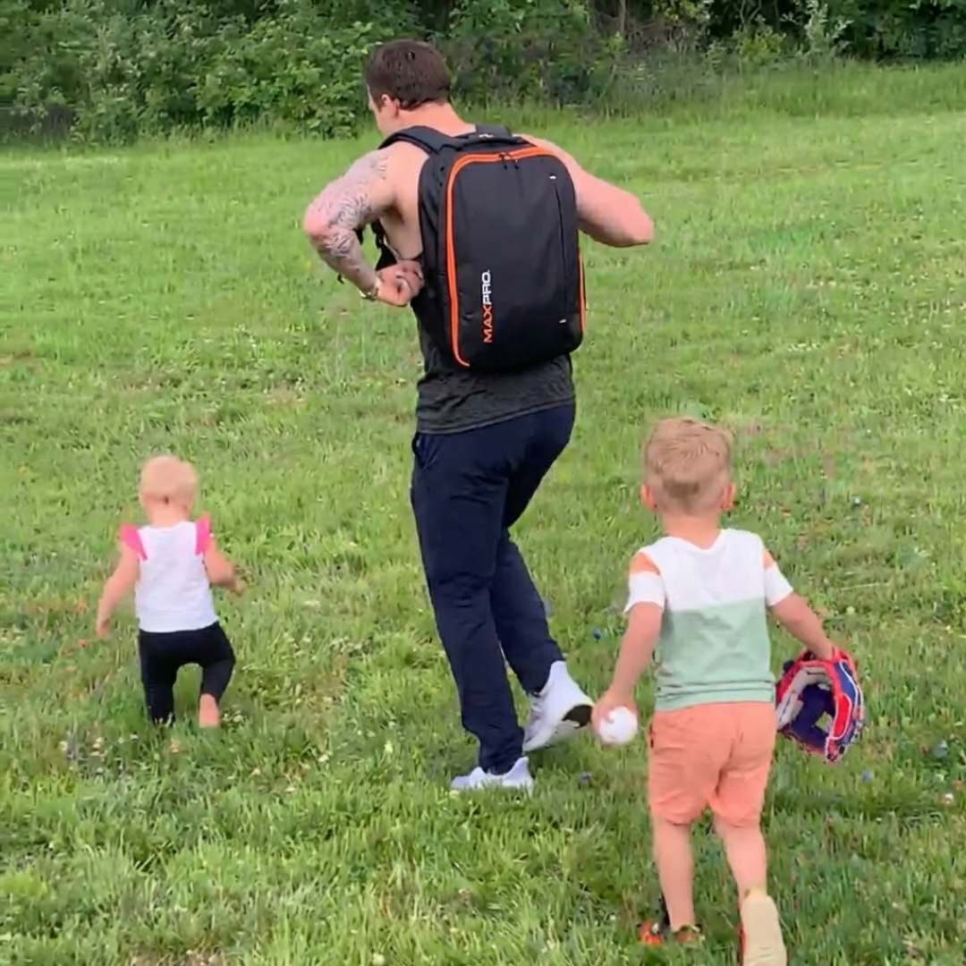Man with a MAXPRO backpack walking with two children in a grassy field