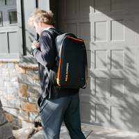 Person wearing a black and orange MaxPro backpack standing in front of a garage door.