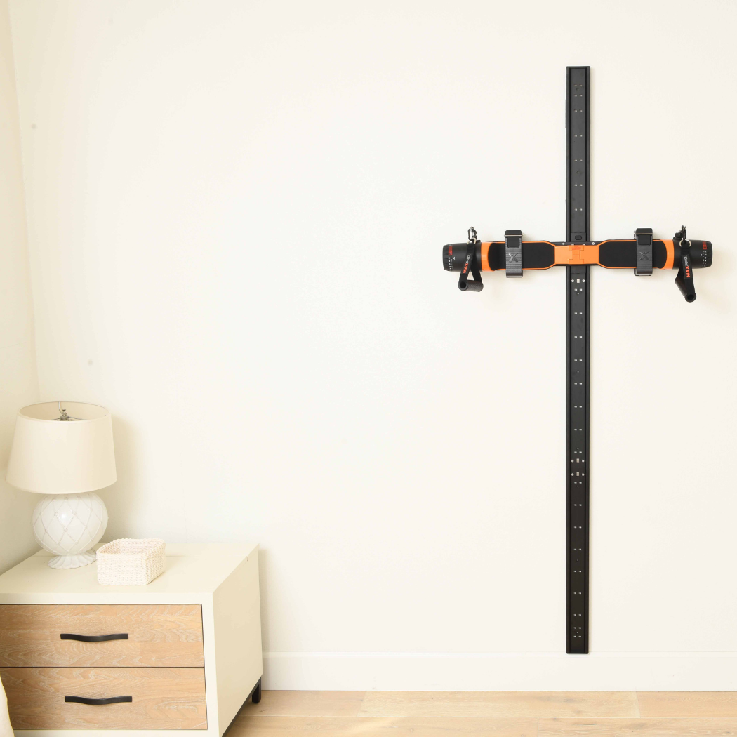 Wall-mounted Slim Line Wall Track against a white wall with a wooden nightstand and lamp in the background. Slim line wall track has orange maxpro in it.