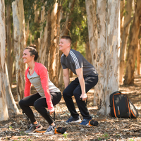 Two people exercising with a MAXPRO outdoors in a forested area with a backpack nearby.