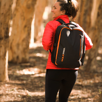 Person wearing a red jacket and black backpack with 'MAXPRO' branding in a forest setting