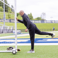 Man stretching on a soccer field with a goalpost and soccer ball in the foreground.