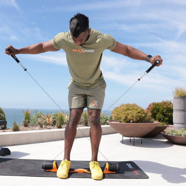 MAXPRO coach performing bent-over reverse fly exercise with portable cable machine on an outdoor patio overlooking the ocean — upper body resistance training for shoulders and back